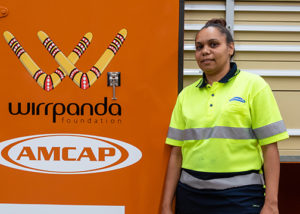 successful female jobseeker in high vis stands infront of wirrpanda foundation and amcap logo sign