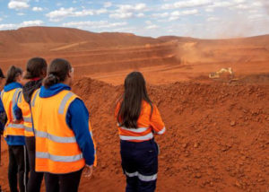 group of women in high vis on red dirt mine site watching dig