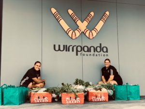 emily and jacinta of the wirrpanda foundation with donation food boxes in front of wirrpanda foundation logo