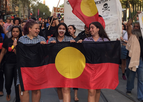 3 teenage girls marching with aboriginal flag